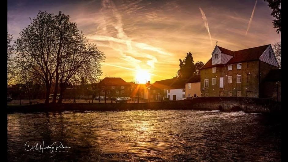 Sunset view of riverside stone buildings and bare trees reflected in water at dusk