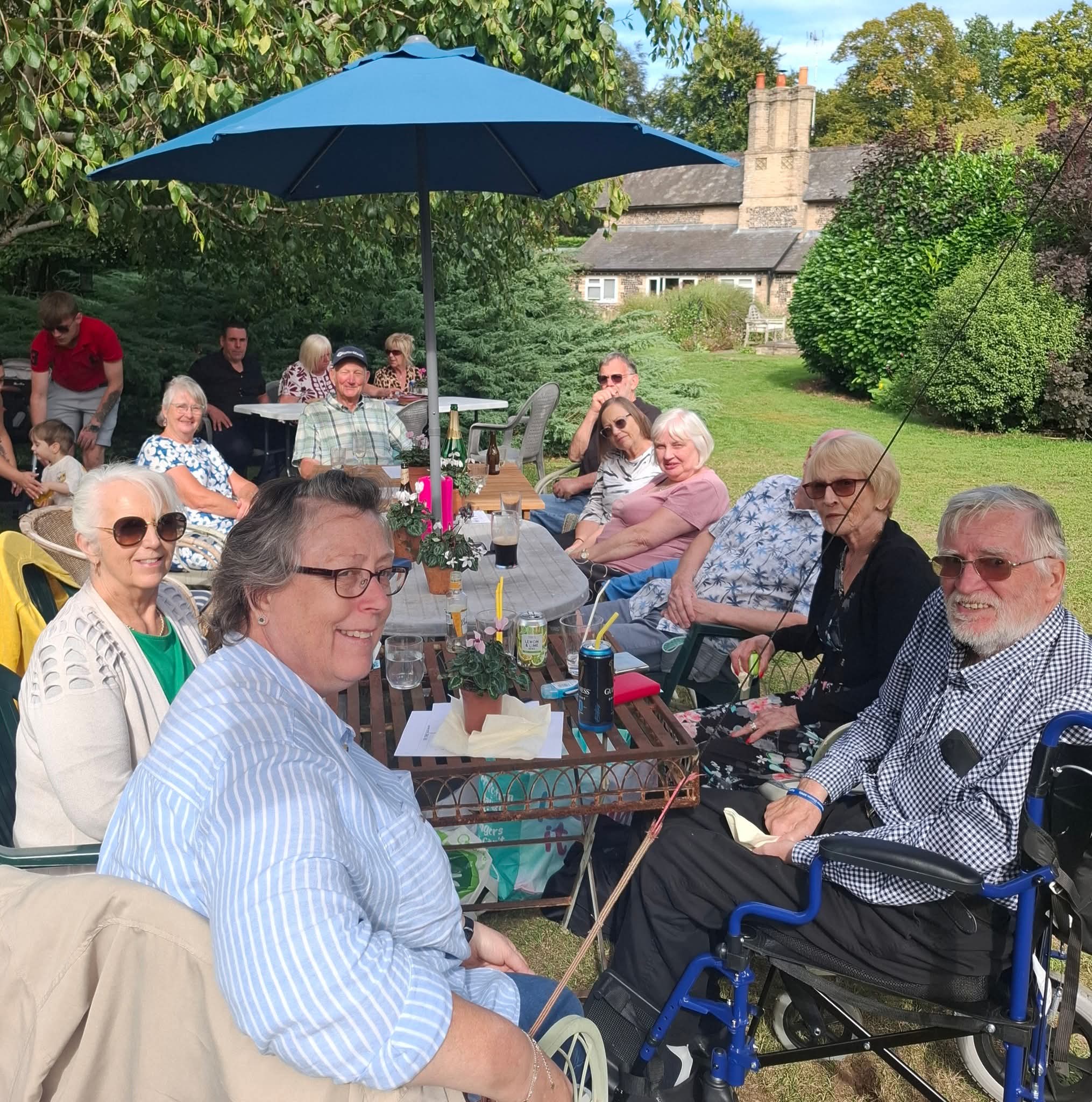 A group of people enjoying an outdoor garden gathering under a blue umbrella at a Masonic lodge event.