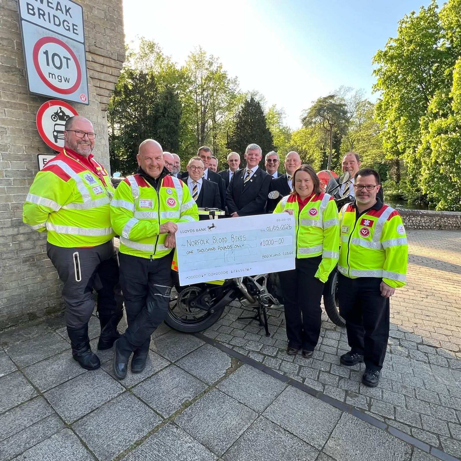 Group of emergency service personnel and officials holding a cheque for Norfolk Blood Bikes charity at Wreak Bridge.